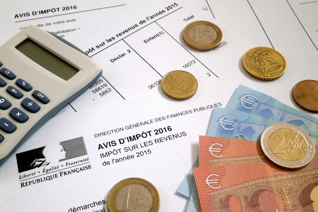 Some euro coins and banknotes as well as a calculator on the top of a French income tax form Avis d'impot sur les revenus