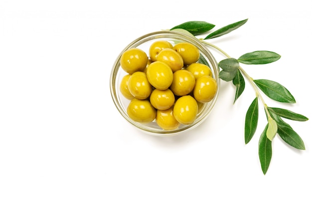 Some fresh olives in a glass bowl and olive branch on the white background.