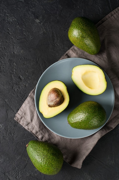 Some fruit of avocado whole and half on plate over dark bckground