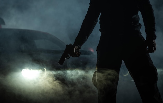 Фото Член банды с пистолетом перед машиной в ночное время незаконная ночная деятельность тема