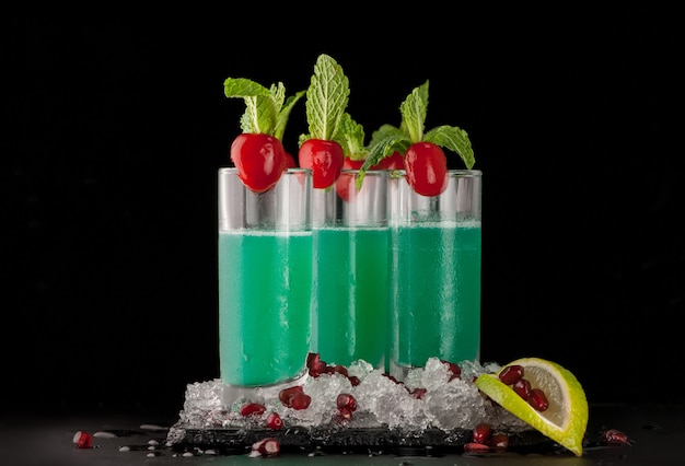 Some glasses with green citrus drink and ice on a black stone on a dark background