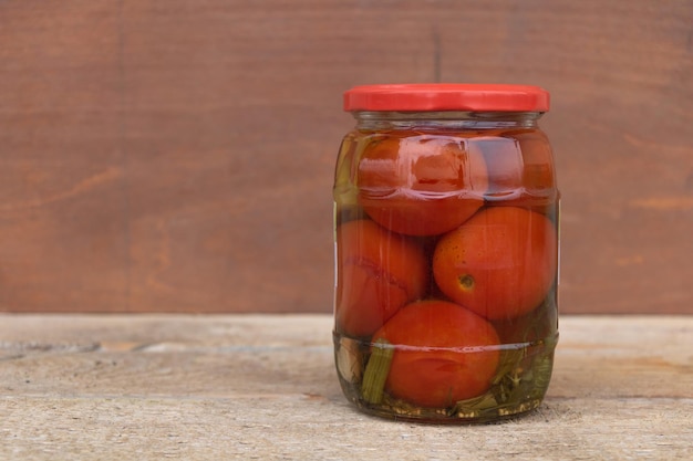 Some marinated tomatoes in a sealed jar on a wooden background