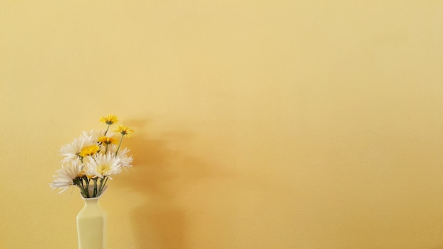 Some minimal flowers in the vase on yellow cement wall background