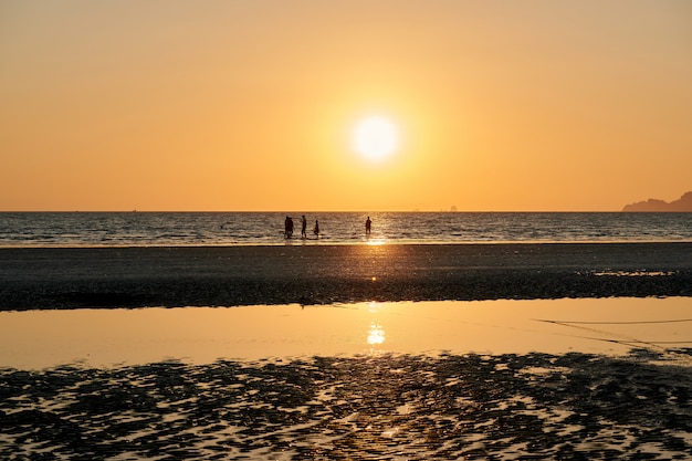 Some people are on a beach during sunset