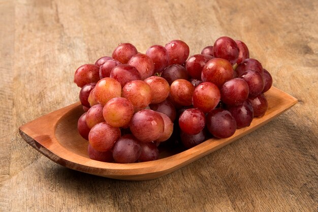 Some red grapes in a wooden pot over a wooden surface seen from above