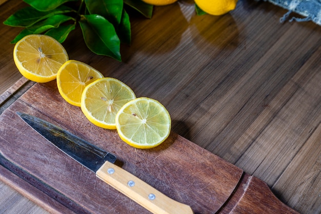 Some slices of lemon cut on a wooden board next to a knife on a rustic background