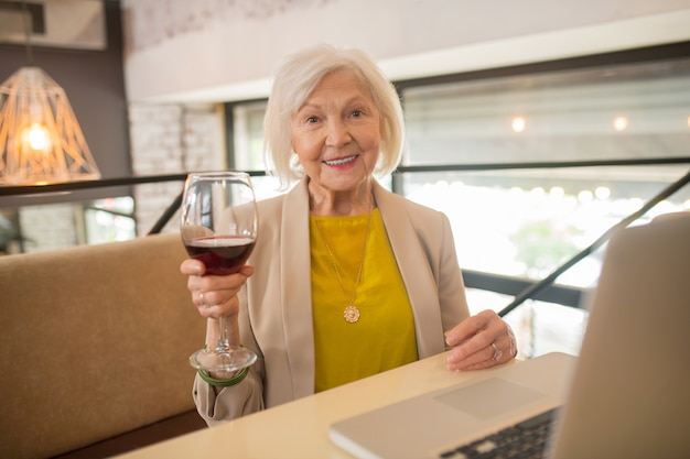 Some wine. Elegant senior woman sitting with a glass of wine in hands