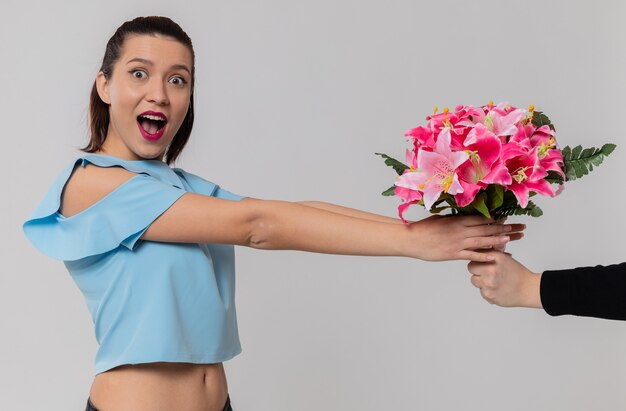 Someone giving bouquet of flowers to excited pretty young woman looking 