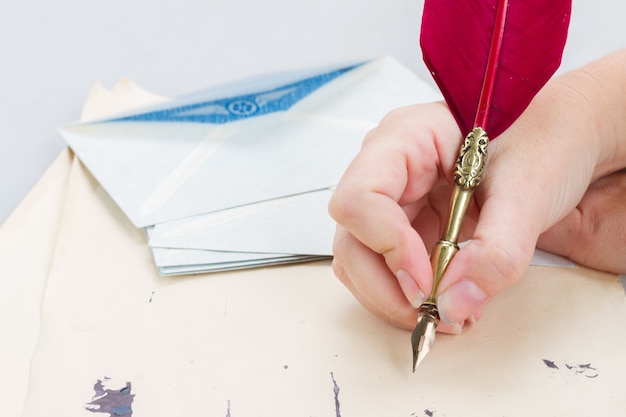 Someone hand holding red feather pen over old papers with ink blots