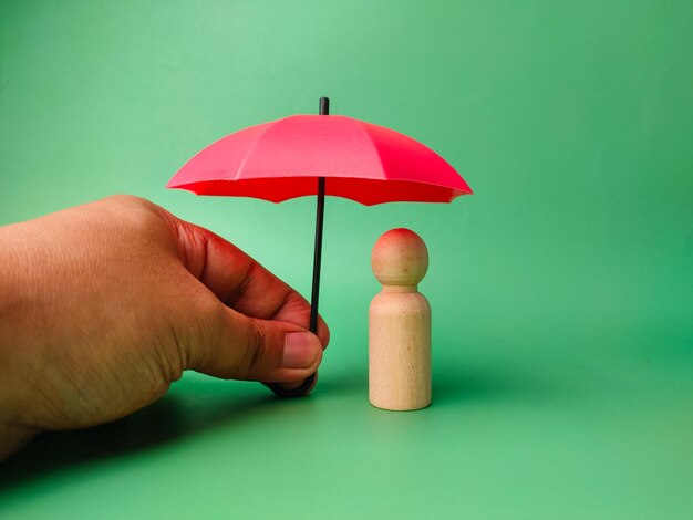 Someone hand holding red umbrella to protect wooden peg doll