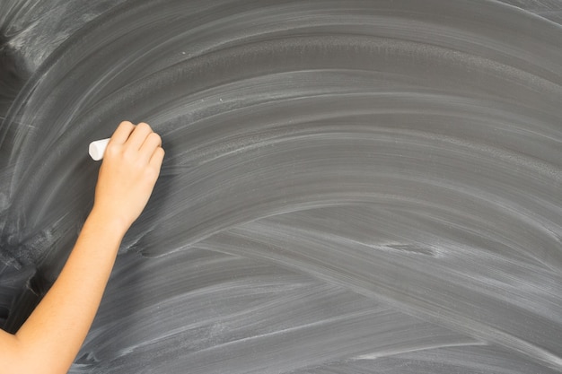 Someone hand with chalk writting on empty black board