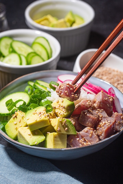 Someone holds piece of tuna fish over Poke Bowl