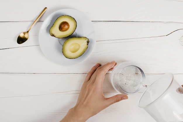 Someone is pouring water into a glass, next to a plate of cut avocado