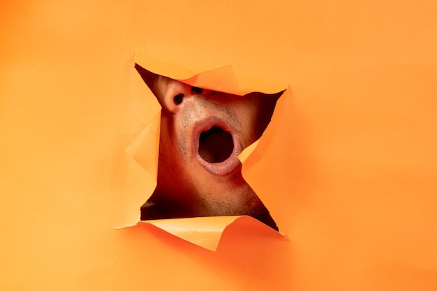 someone peeking out from behind the orange torn paper background