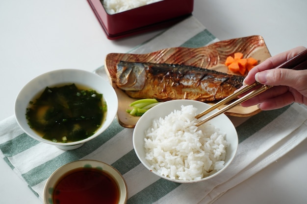 Someone using chopsticks trying to pick cooked rice served with a grilled saba