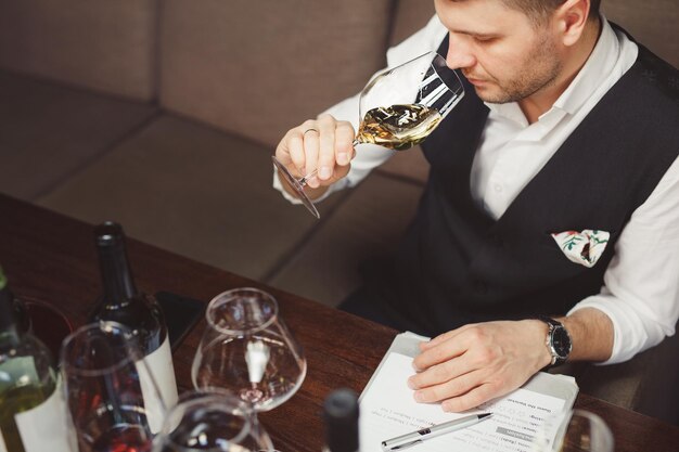 Sommelier ruikt dure witte wijn gegoten in elegant wijnglas zittend aan tafel in restaurant