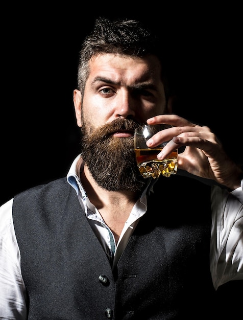 Il sommelier assaggia una bevanda costosa uomo d'affari barbuto in abito elegante con un bicchiere di whisky degustazione uomo con la barba tiene un bicchiere di brandy