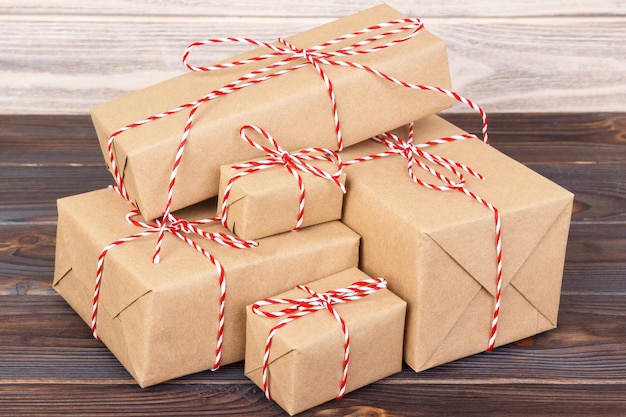 Foto sommige papieren pakketten kerstcadeau dozen verpakt met kraftpapier en gebonden met rood wit bakker touw in een donkere houten tafel kerstcadeau dozen