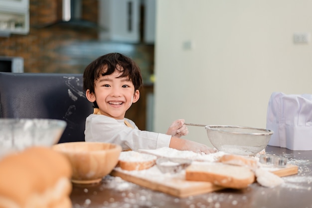 Son cooking food. Preparing an ingredient with flour and bread. Kid daily lifestyle at home. Asian family in the kitchen.