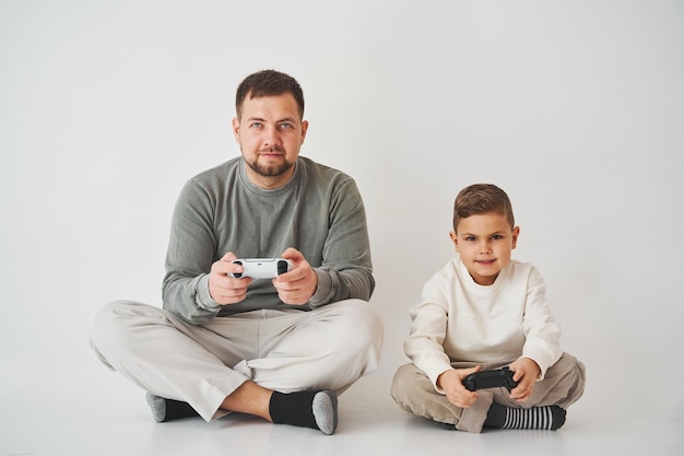 Son and dad play console games with gamepad boy and his father\
spend time togerher and playing computer games