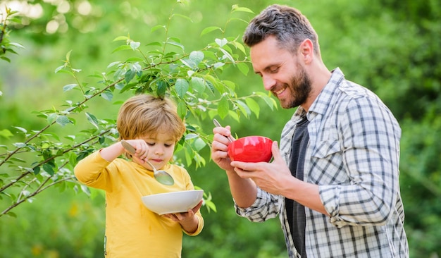 Son and father eating outdoor healthy food and dieting Dairy products weekend morning breakfast Happy family together happy fathers day Little boy with dad eat cereal Healthy food for success