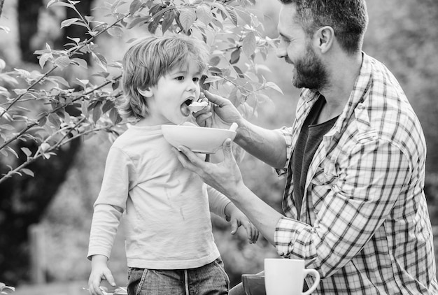 Son and father eating outdoor Morning breakfast Tasty food healthy food and dieting Dairy products happy fathers day Little boy with dad eat cereal family rest time Weekend with family