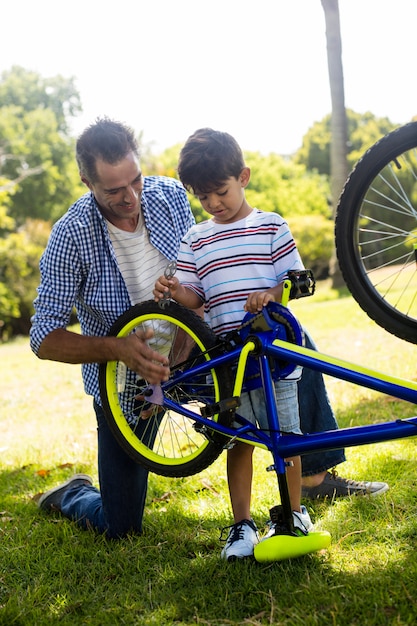 Figlio e padre che riparano la loro bicicletta in parco