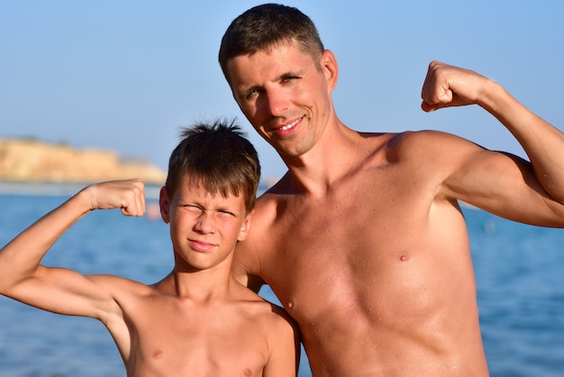 Son and father show muscles at sea