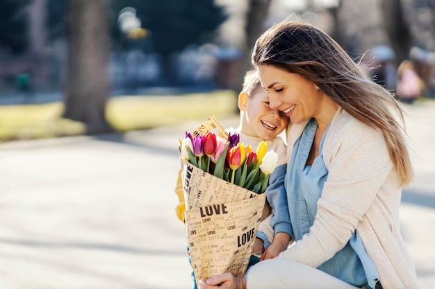 A son hugging his mother in a park while mother holding flowers she got on mother39s day