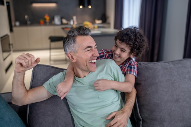 Son hugging laughing father sitting on sofa