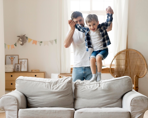 Фото Сын прыгает на диване и удерживается отцом
