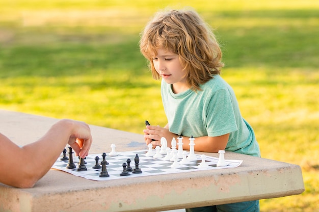 Son kid playing chess on table in park outdoor with his father childhood