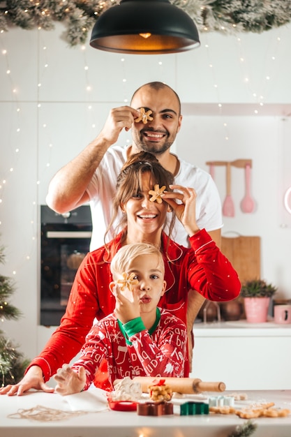 Сын, мама и папа пекут рождественские торты на кухне, улыбаясь, глядя в камеру