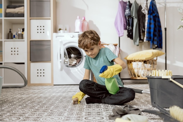 A son mops the floor at home using yellow rubber gloves a brush and liquid