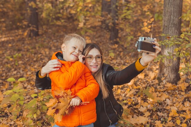 Son and mother are taking selfie on camera in autumn park single parent leisure and fall season