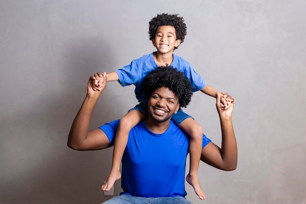 Son sitting on father\'s shoulder on gray background happy afro\
father and son