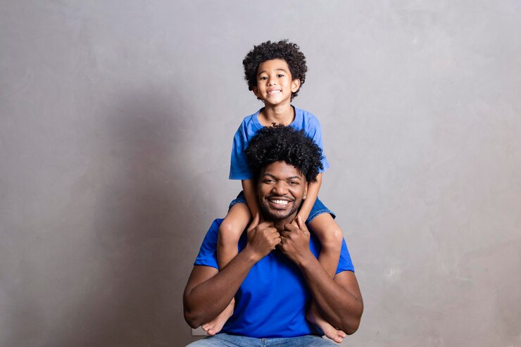 Son sitting on father's shoulder on gray background Happy afro father and son