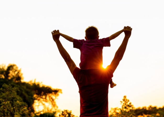 Figlio seduto sulle spalle del padre in estate in natura all'immagine della silhouette beautiful sunset