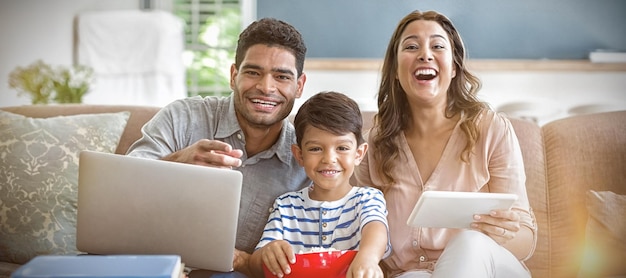 Son watching television while father and mother using laptop and digital tablet at home