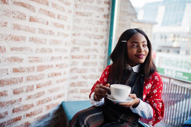 Sonfident young african american woman in smart casual wear at cafe with cup of hot drink in hand