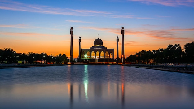 Songkhla Central Mosque in day to night with colorful skies at sunset and the lights of the mosque and reflections in the water in landmark landscape concept