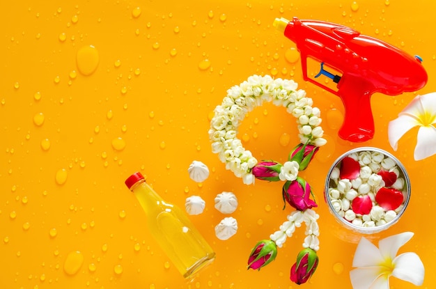 Songkran festival background with jasmine garland water gun\
flowers in water bowl scented water and marly limestone put on\
clear mirror that have wet yellow background below