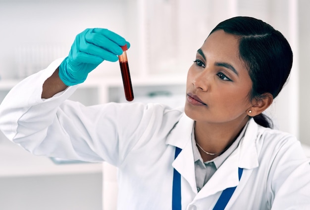 Presto saprò cosa c'è in questo sangue inquadratura ritagliata di una giovane e attraente scienziata che ispeziona una provetta piena di sangue mentre lavora in un laboratorio