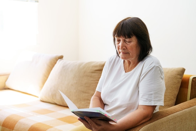 Soothing reading portrait of thoughtful elderly woman reading her favorite literature in cozy home s...