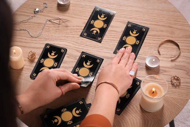 Soothsayer predicting future with tarot cards at wooden table closeup