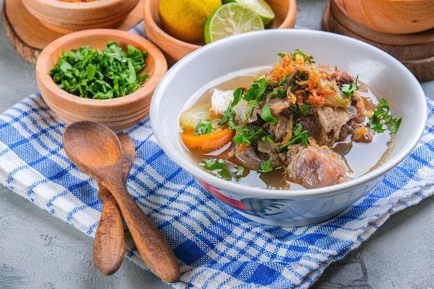 Sop buntut of ossenstaartsoep wordt geserveerd in een witte kom op een rustieke grijze achtergrond. Indonesische traditionele culinaire