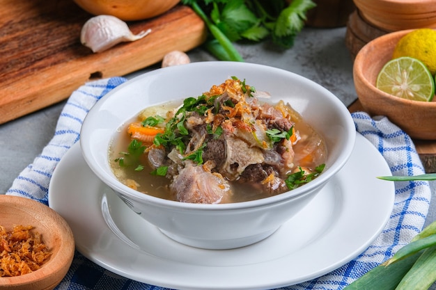 Sop buntut or oxtail soup is served in white bowl on rustic grey background. indonesian traditional culinary