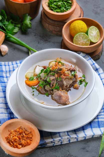 Sop buntut or oxtail soup is served in white bowl on rustic grey background. indonesian traditional culinary