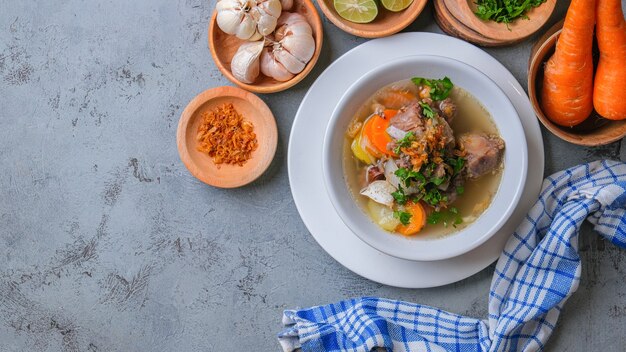 Sop buntut or oxtail soup is served in white bowl on rustic grey background. indonesian traditional culinary