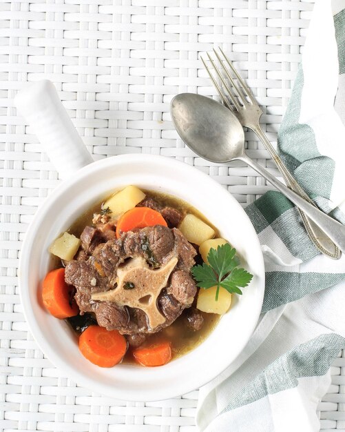 Sop Buntut or Oxtail Soup Served in White Bowl on White Woven Table Top View